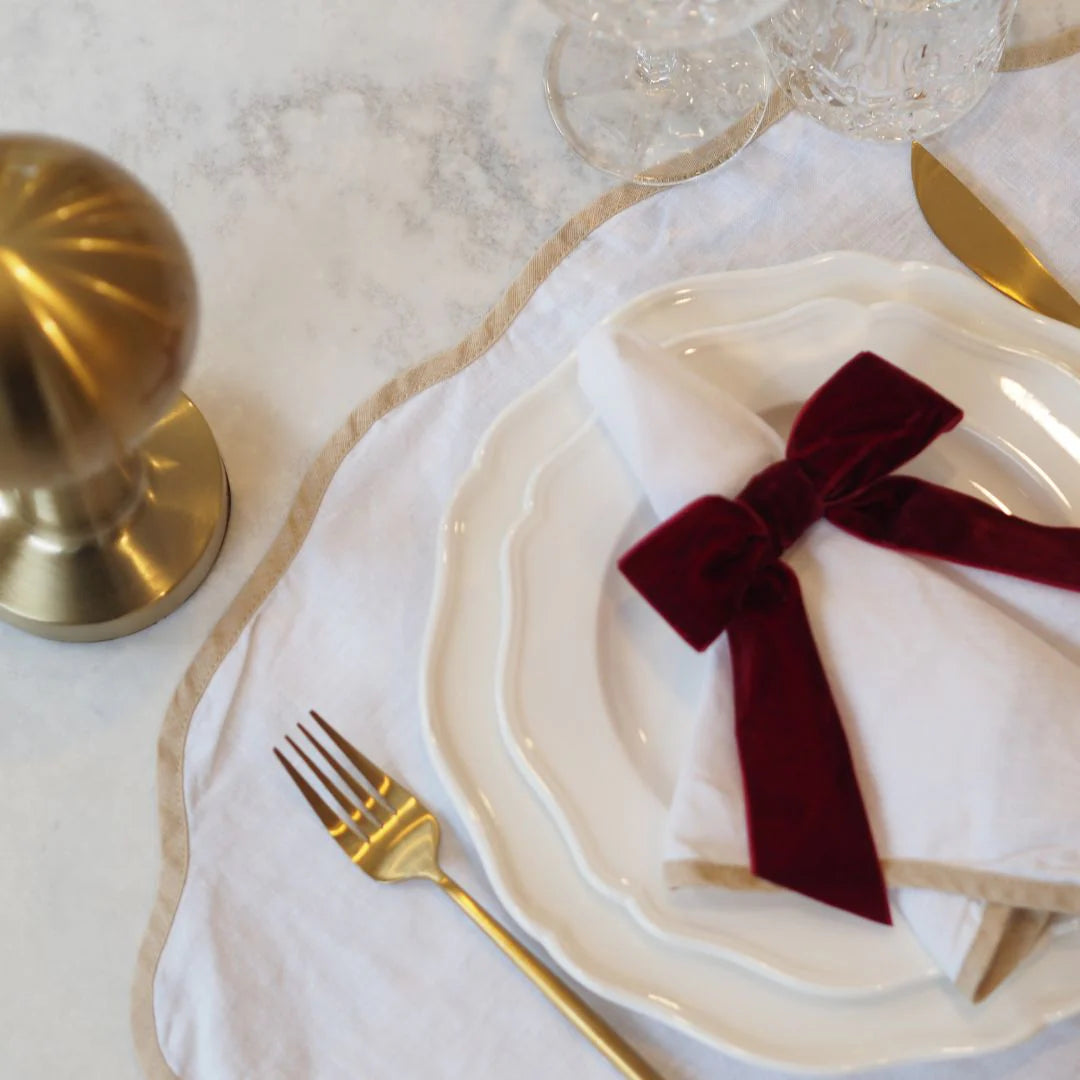 Tablescape Dining table setting with white plates, gold cutlery, and a red bow on a marble surface.
