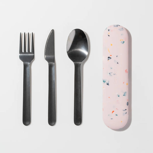A flat-lay of a four-piece metal cutlery set with a pink terrazzo-patterned protective case on a clean white background.

