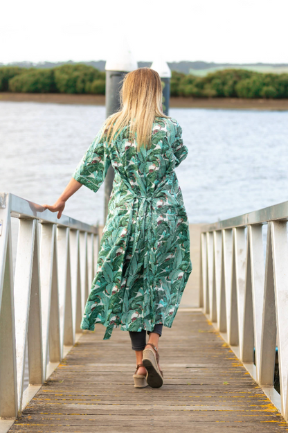Woman in a green floral dress walking on a wooden dock by a lake.