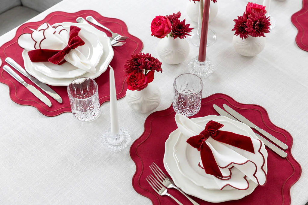 Tablescape Dining table set with red placemats, napkins, and centerpieces on a white tablecloth.