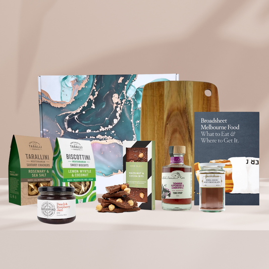 The Flavour Favourites gourmet gift hamper featuring tarallini biscuits, a Melbourne food guide book, a Miei branded chopping board, Koko Black hazelnut bits, Triffid Tonic, Gewürzhaus hot chocolate, Daylesford jam and Biscottini lemon myrtle biscuits.